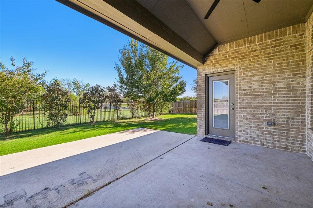 284 Goliad Trail, Forney, TX 75126 Covered concrete patio featuring brick exterior walls, a ceiling fan, and metal perimeter fencing bordering a lawn