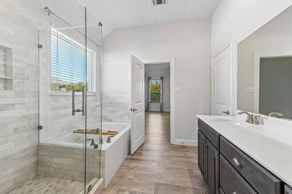 284 Goliad Trail, Forney, TX 75126 Bathroom featuring a glass-enclosed shower with tiled surround, separate soaking tub, wood-finish flooring, dark-toned cabinetry, and a countertop with an integrated sink