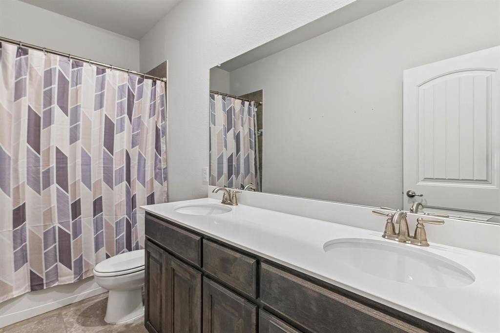 284 Goliad Trail, Forney, TX 75126 Dual-sink vanity with a solid-surface countertop, dark wood-finish cabinetry, a full-width wall mirror, and metallic finish hardware