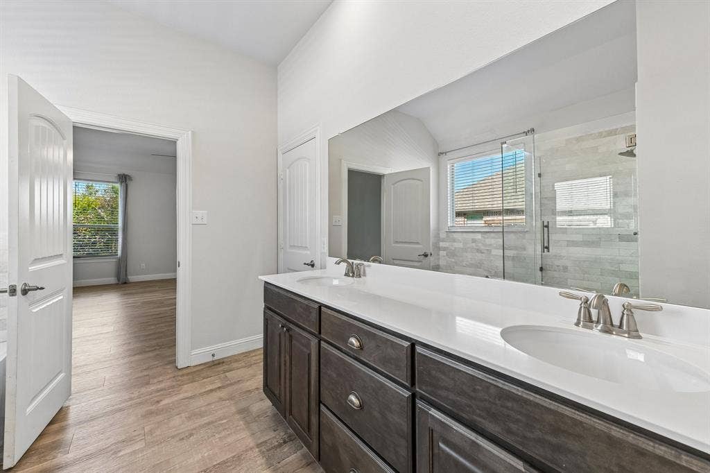 284 Goliad Trail, Forney, TX 75126 Bathroom vanity featuring dark-toned cabinetry, dual undermount sinks, and a solid-surface countertop with a full-width mirror