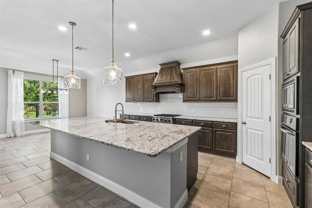 284 Goliad Trail, Forney, TX 75126 Kitchen featuring dark wood cabinetry, expansive stone-surface center island, built-in wall oven and microwave, stone-finish tile flooring, and decorative glass pendant lighting