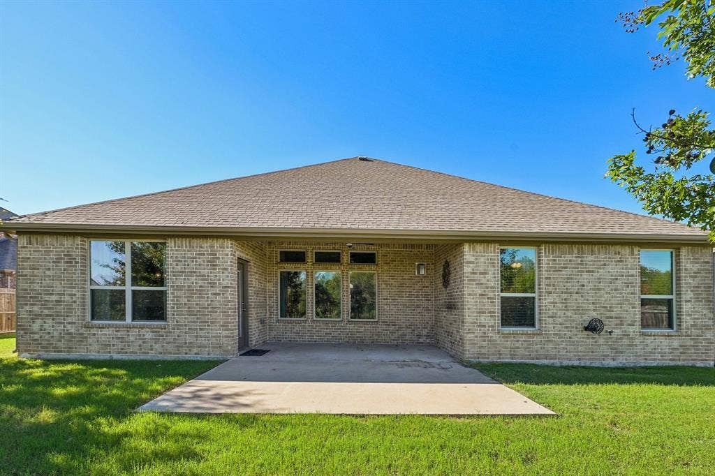 284 Goliad Trail, Forney, TX 75126 Rear exterior featuring a brick facade, concrete patio, multi-pane windows, and a hip roof
