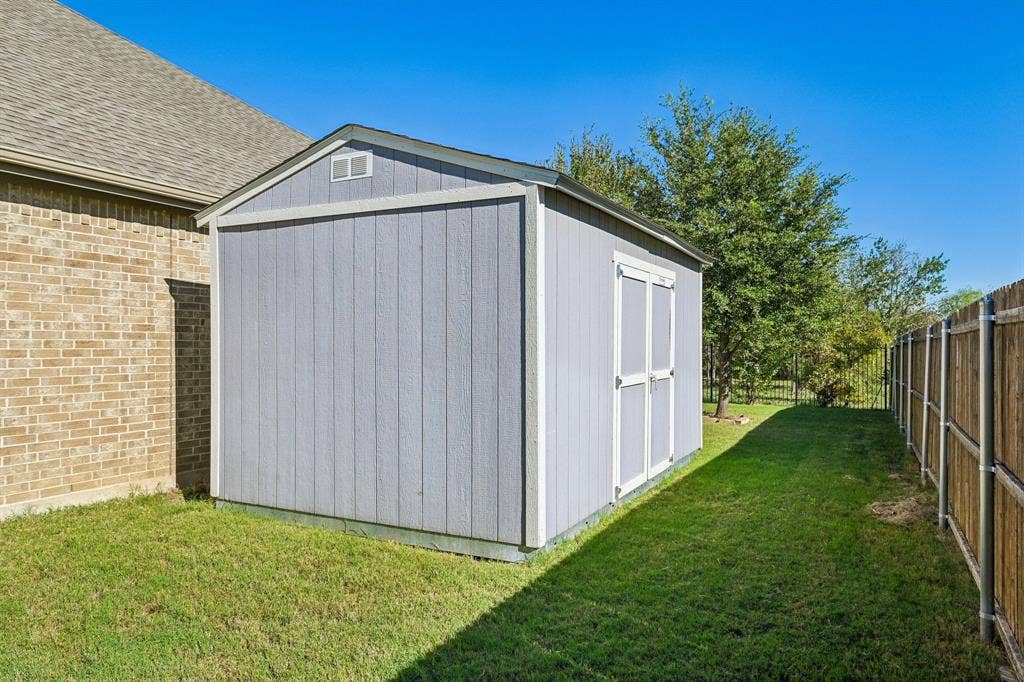 284 Goliad Trail, Forney, TX 75126 Exterior storage structure with vertical siding, gable roof, double-door entry, and wood fencing