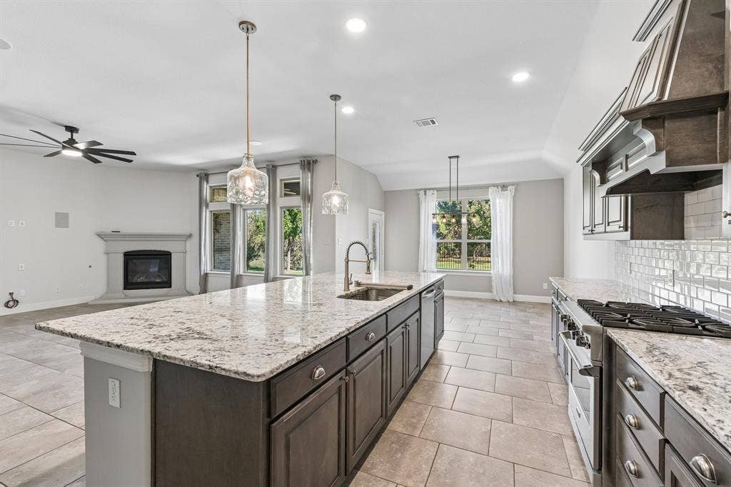 284 Goliad Trail, Forney, TX 75126 Kitchen featuring a large central island with light-toned stone countertops, dark cabinetry, tile flooring, built-in stainless steel appliances, and a tiled backsplash