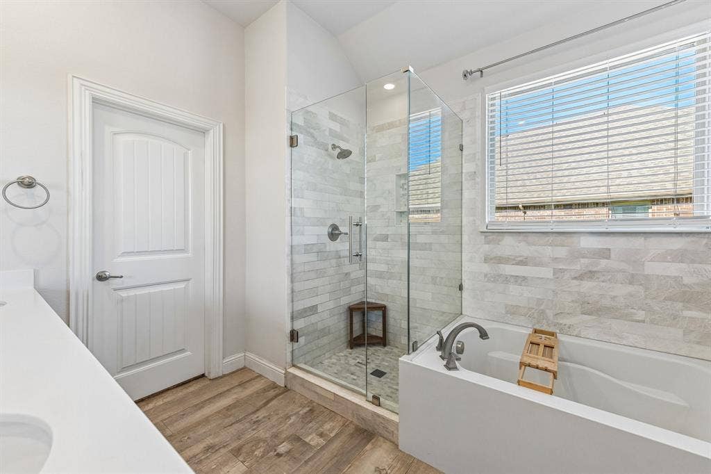 284 Goliad Trail, Forney, TX 75126 Glass-enclosed shower with horizontal wall tile and stone-finish floor, deep soaking tub with wall-mounted faucet, and wood-finish flooring