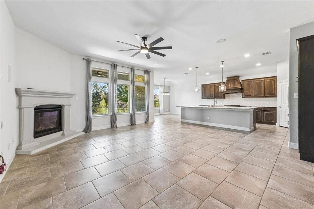 284 Goliad Trail, Forney, TX 75126 Open-concept interior featuring large-format tile flooring, a stone-finish fireplace surround, dark wood cabinetry with a coordinating range hood, and a kitchen island with stone-finish countertops