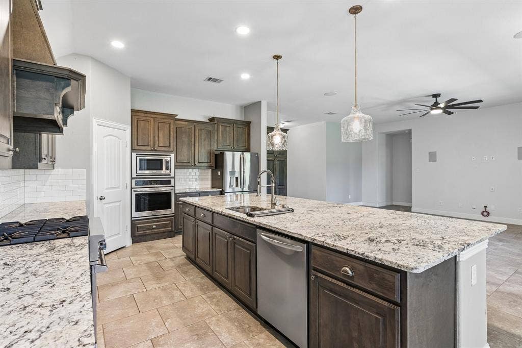 284 Goliad Trail, Forney, TX 75126 Kitchen featuring stone countertops, dark-finish cabinetry, stainless steel double wall ovens, a large central island, and glass pendant lighting