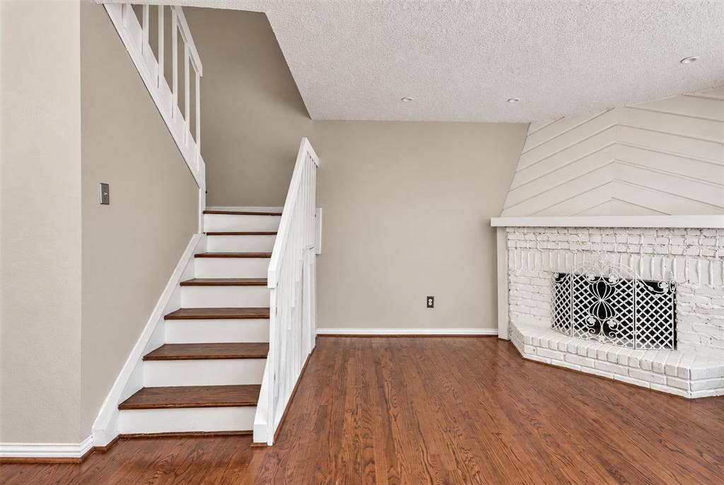 895 Dublin Drive, #4, Richardson, TX 75080 Wood-finish flooring, staircase with white railing and wood-finish treads, and a white painted brick fireplace with geometric wall paneling