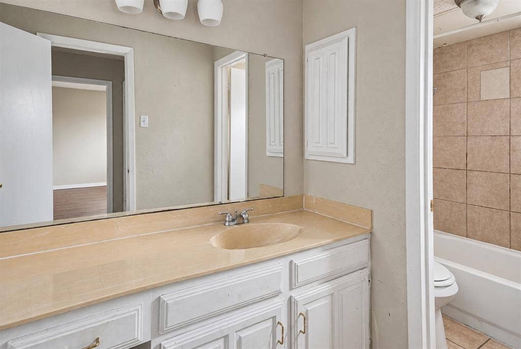 895 Dublin Drive, #4, Richardson, TX 75080 Bathroom vanity featuring white cabinetry, a solid-surface countertop with an integrated oval sink, a large wall-mounted mirror, and a three-light fixture