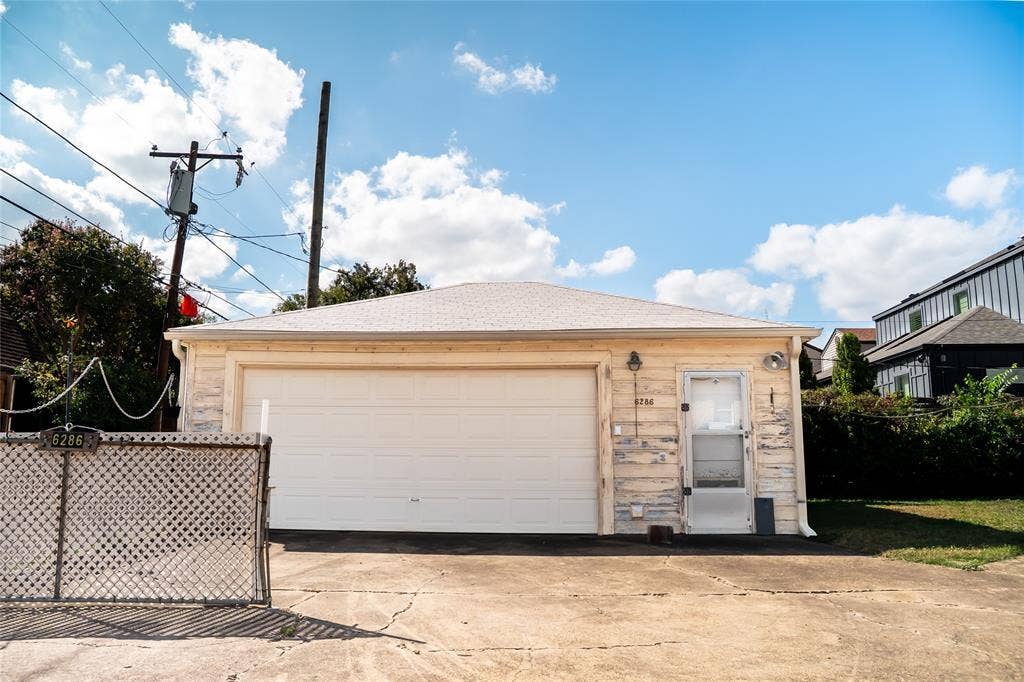 Detached garage featuring a shingle roof, paneled garage door, and a separate side-entry door, situated on a paved concrete driveway with an integrated lattice screen
