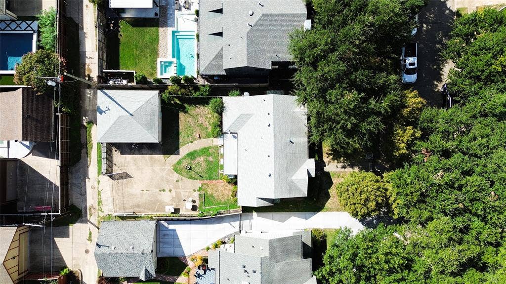 Aerial perspective of property featuring a detached garage, concrete driveway, mature landscaping, and grass lawn