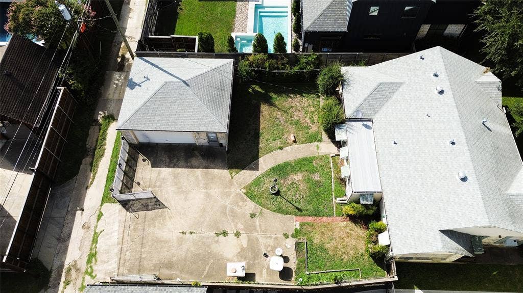 Aerial perspective of a property featuring a detached garage, expansive concrete driveway, gated perimeter, and lawn area