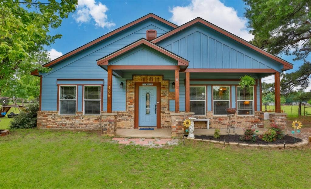 Single-story exterior featuring blue vertical siding, brick veneer foundation, front-facing gabled roofline, and a covered porch supported by wood-finish posts