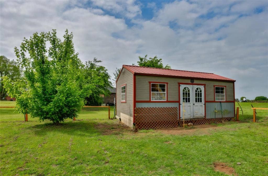 Detached storage building with metal roofing, vinyl siding, double entry doors, and lattice skirting, situated on a fenced lot