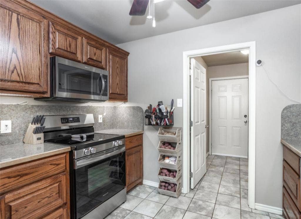 Kitchen featuring raised-panel wood cabinetry, stainless steel range with overhead microwave, stone-finish countertops, and ceramic tile flooring