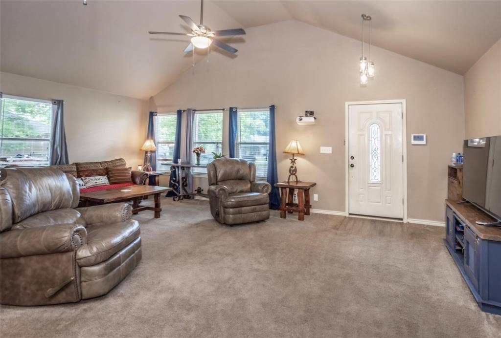 Vaulted ceilings featuring a central ceiling fan, multiple windows with neutral trim, and an entry door with an inset glass panel
