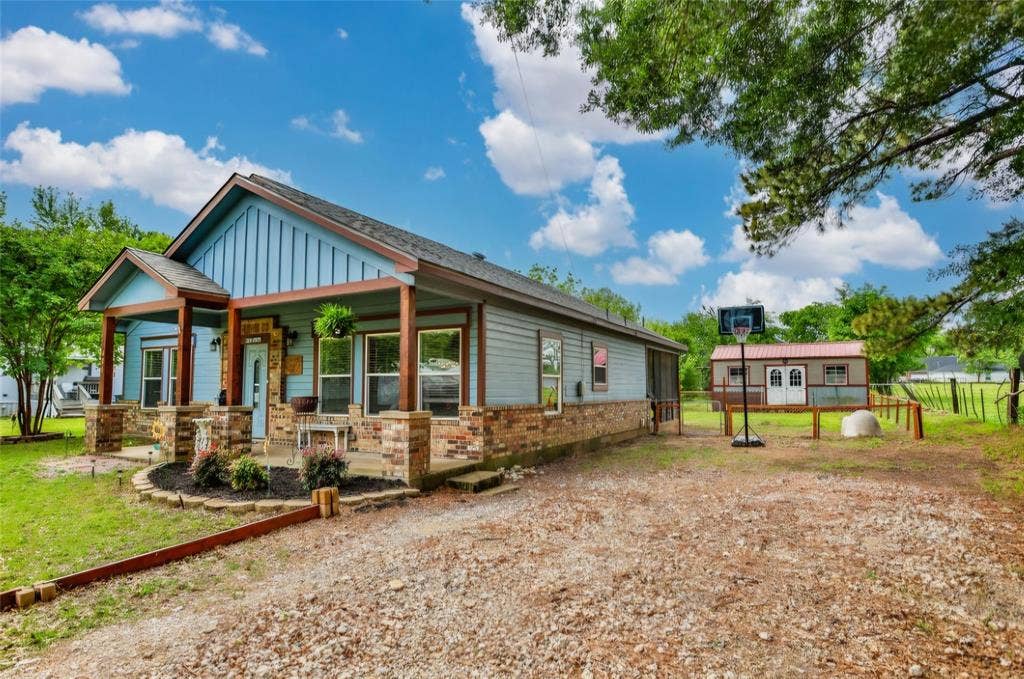 Single-story residence featuring blue vertical siding, a stone veneer foundation, a covered front porch with wood support columns, and a detached storage structure