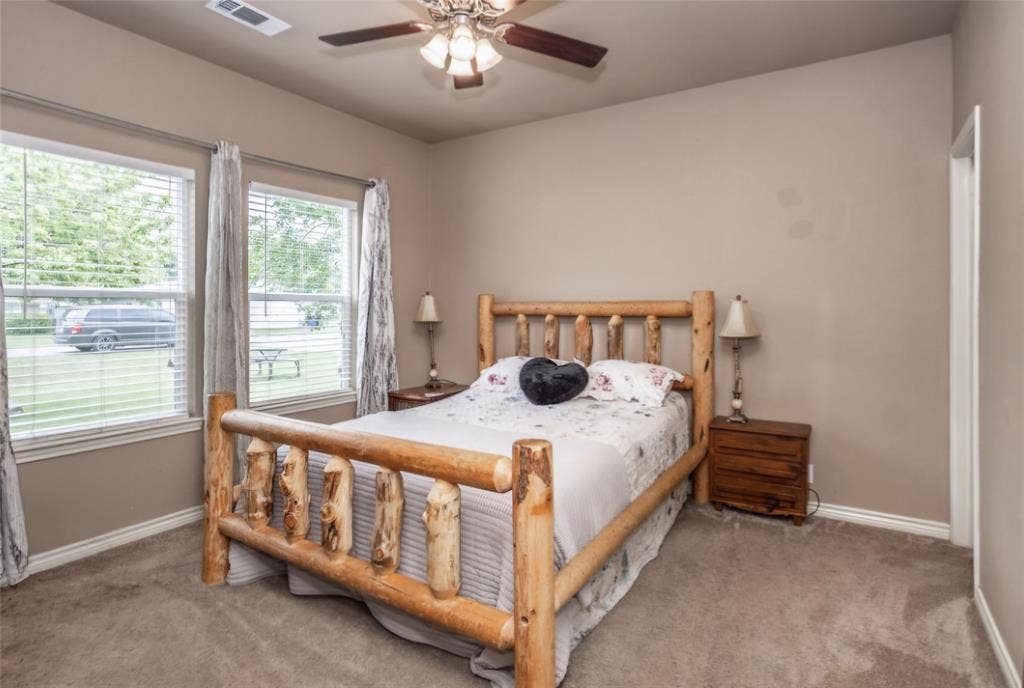 Neutral-toned interior room featuring wall-to-wall carpeting, dual windows, and a multi-blade ceiling fan with integrated lighting