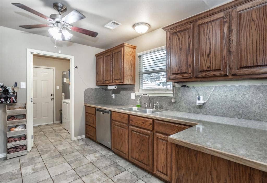 Kitchen featuring stained wood cabinetry, stone-finish countertops, stainless steel dishwasher, double-basin sink, and tile flooring