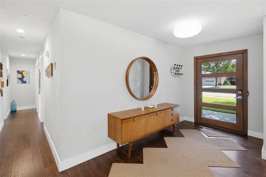 A welcoming entryway features a contemporary wood-framed front door with four glass panels, rich flooring, and clean, modern finishes. Natural light brightens the foyer, while the adjoining hallway provides access to the home's bedrooms and bathrooms, creating a comfortable transition between the main living areas and private spaces.