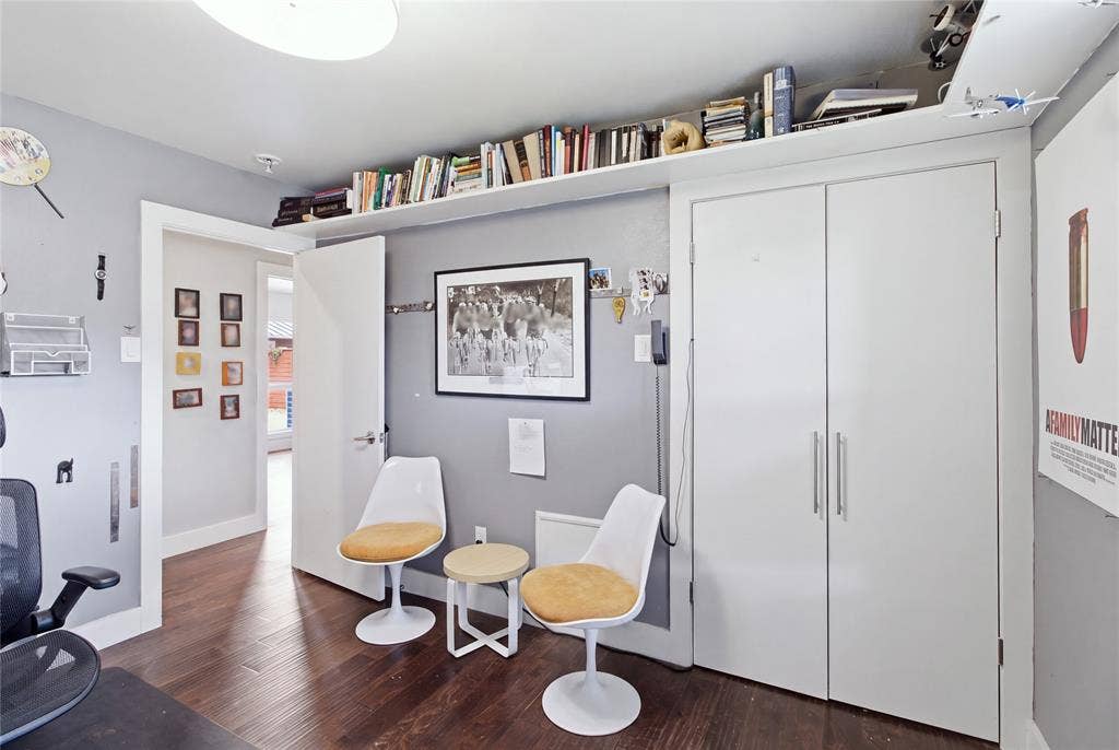 Another perspective of the secondary bedroom currently used as a home office, highlighting the double-door closet, extensive upper-wall shelving, and room for additional seating. The versatile layout offers flexibility for a bedroom, home office, or personal retreat.