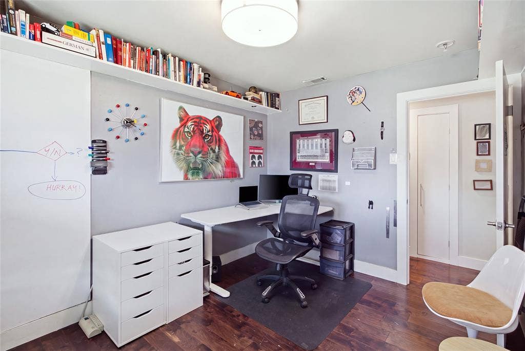 Currently arranged as a home office, this secondary bedroom demonstrates the home's flexible living spaces. Rich flooring, contemporary lighting, and extensive upper-wall shelving create a distinctive workspace, while a large window brings in natural light. The room can easily serve as a traditional bedroom, study, or creative retreat to suit your needs.