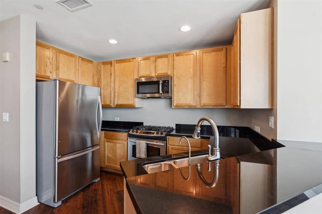 500 Throckmorton Street, #2702, Fort Worth, TX 76102 Kitchen featuring wood-finish cabinetry, black stone countertops, stainless steel appliances, a gas range, and a double-basin stainless steel sink with a high-arc faucet