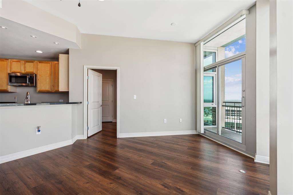 500 Throckmorton Street, #2702, Fort Worth, TX 76102 Open-concept living space featuring wood-finish flooring, floor-to-ceiling windows, access to a private balcony, and a kitchen with wood cabinetry and a breakfast bar