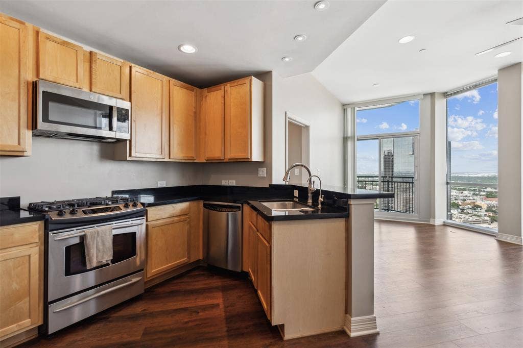 500 Throckmorton Street, #2702, Fort Worth, TX 76102 Kitchen featuring light-tone wood cabinetry, dark stone countertops, stainless steel appliances, wood-finish flooring, and floor-to-ceiling windows