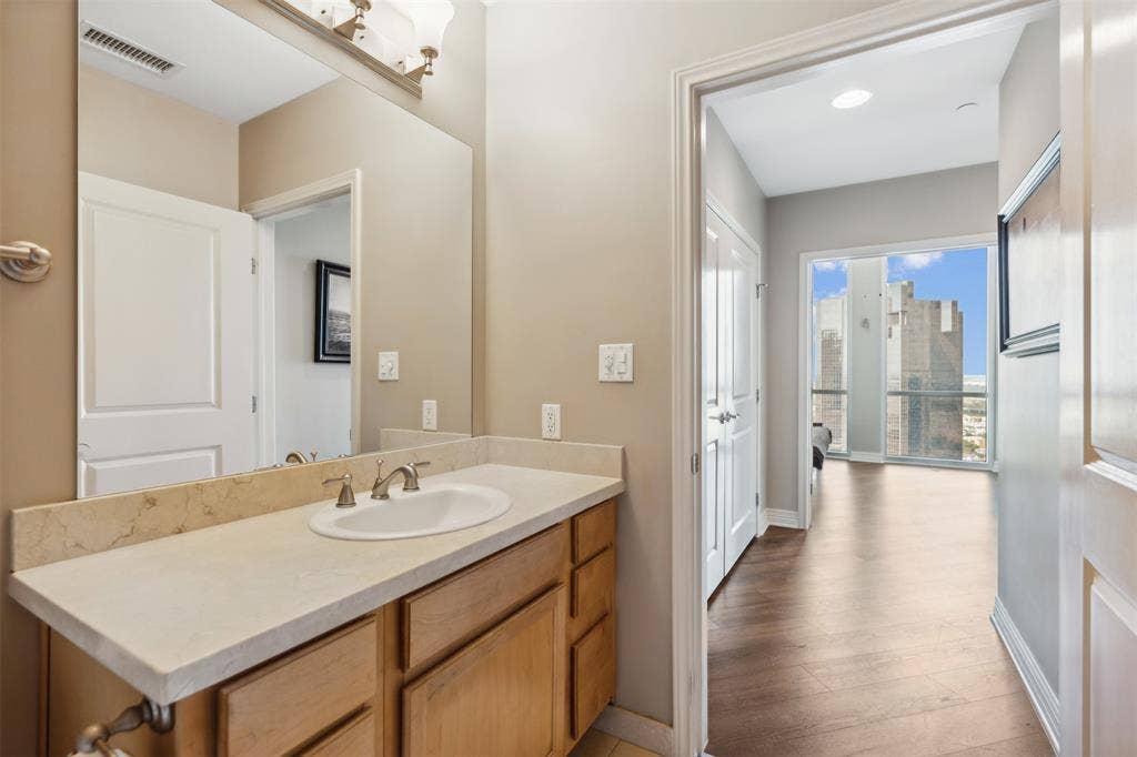 500 Throckmorton Street, #2702, Fort Worth, TX 76102 Bathroom featuring a wood-finish vanity with a stone countertop, integrated sink, and large wall-mounted mirror, paired with wood-finish flooring throughout the interior