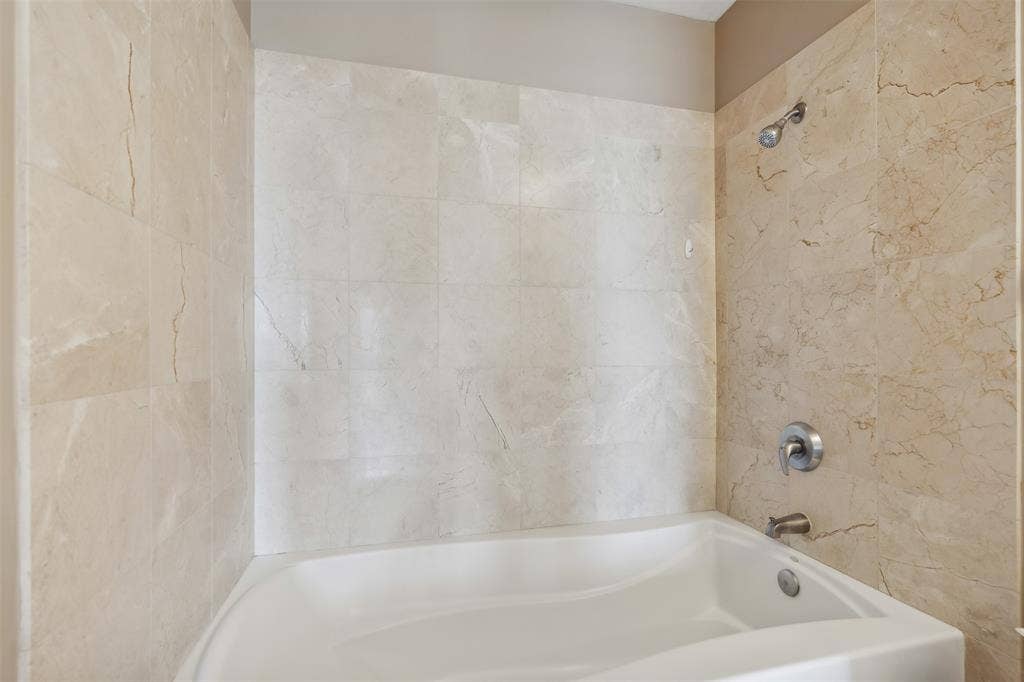 500 Throckmorton Street, #2702, Fort Worth, TX 76102 Bathtub with a white acrylic surround, wall-mounted polished chrome fixtures, and neutral stone-finish tile wall cladding
