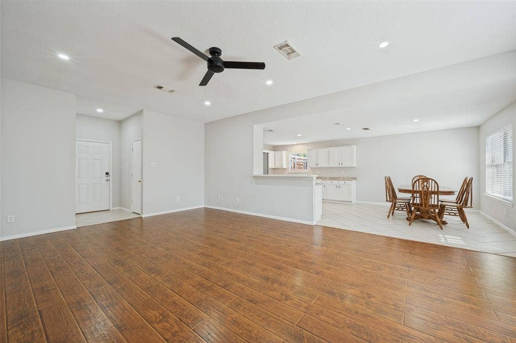 Open-concept interior featuring wood-finish flooring, a matte black ceiling fan, recessed lighting, and white cabinetry in the kitchen
