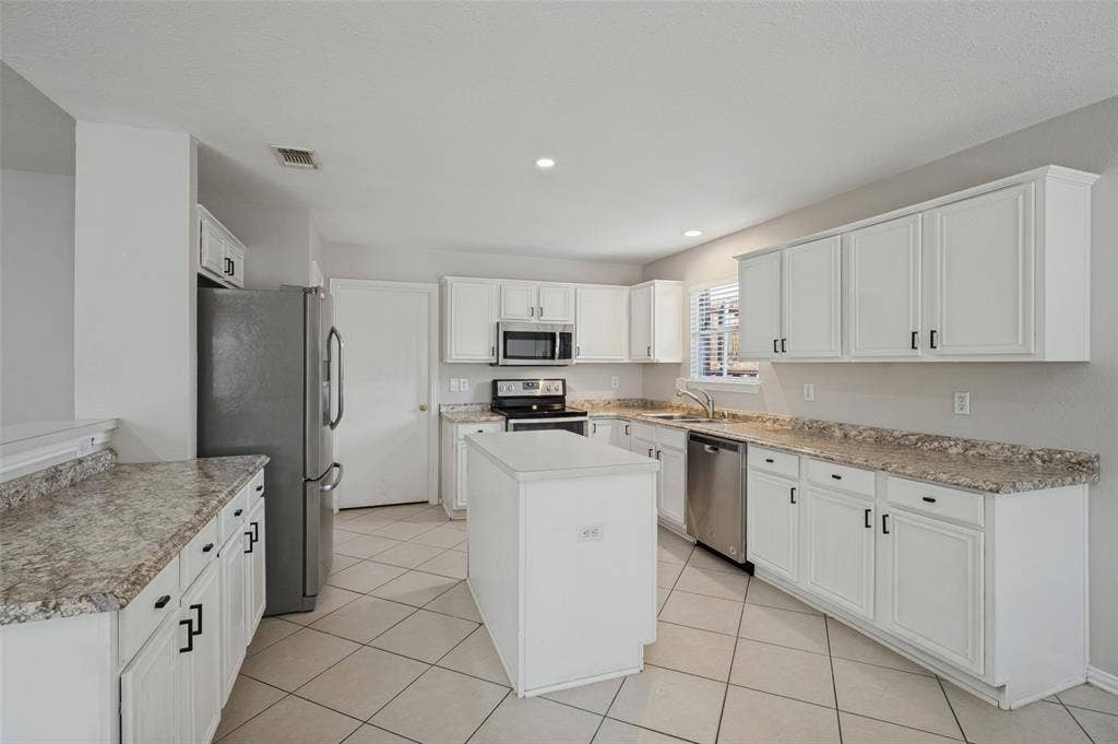 Kitchen featuring white cabinetry, stone-patterned laminate countertops, a central island, stainless steel appliances, and tile flooring