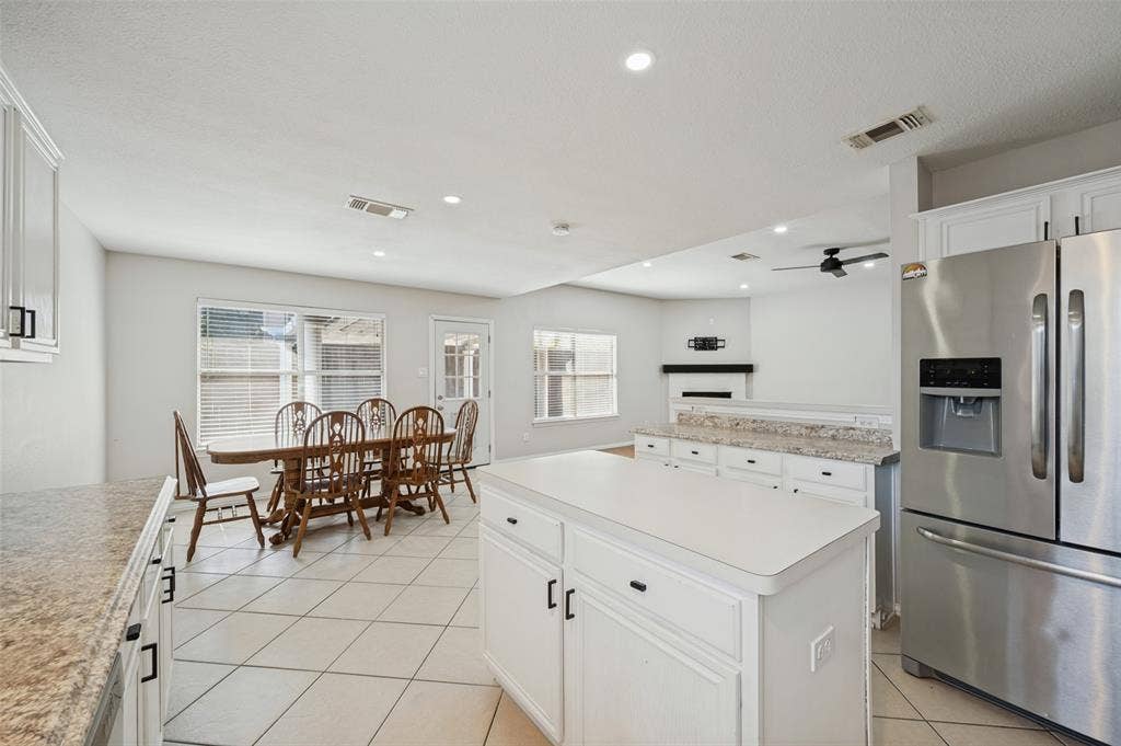 Kitchen featuring white cabinetry, center island, solid-surface countertops, tile flooring, and stainless steel refrigerator