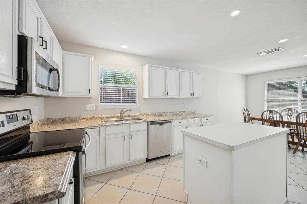 Kitchen featuring white cabinetry, stone-finish countertops, stainless steel appliances, a central island, and tile flooring