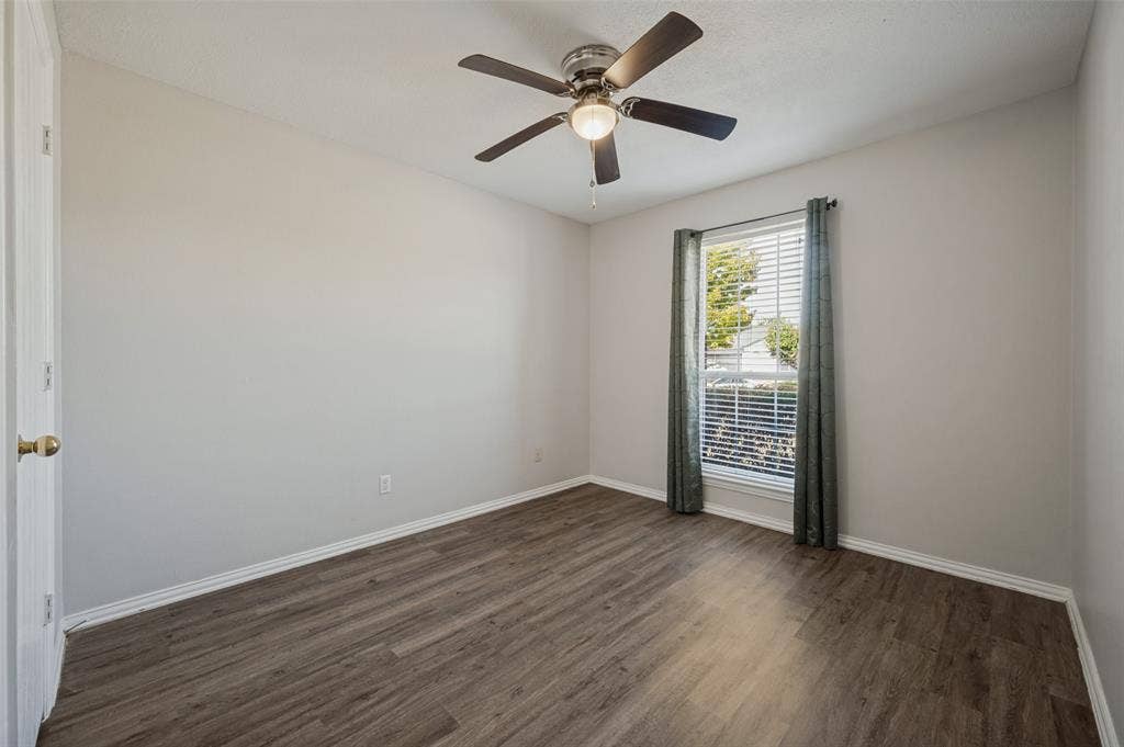 Neutral interior room featuring wood-finish flooring, a ceiling fan with integrated lighting, and a single-pane window