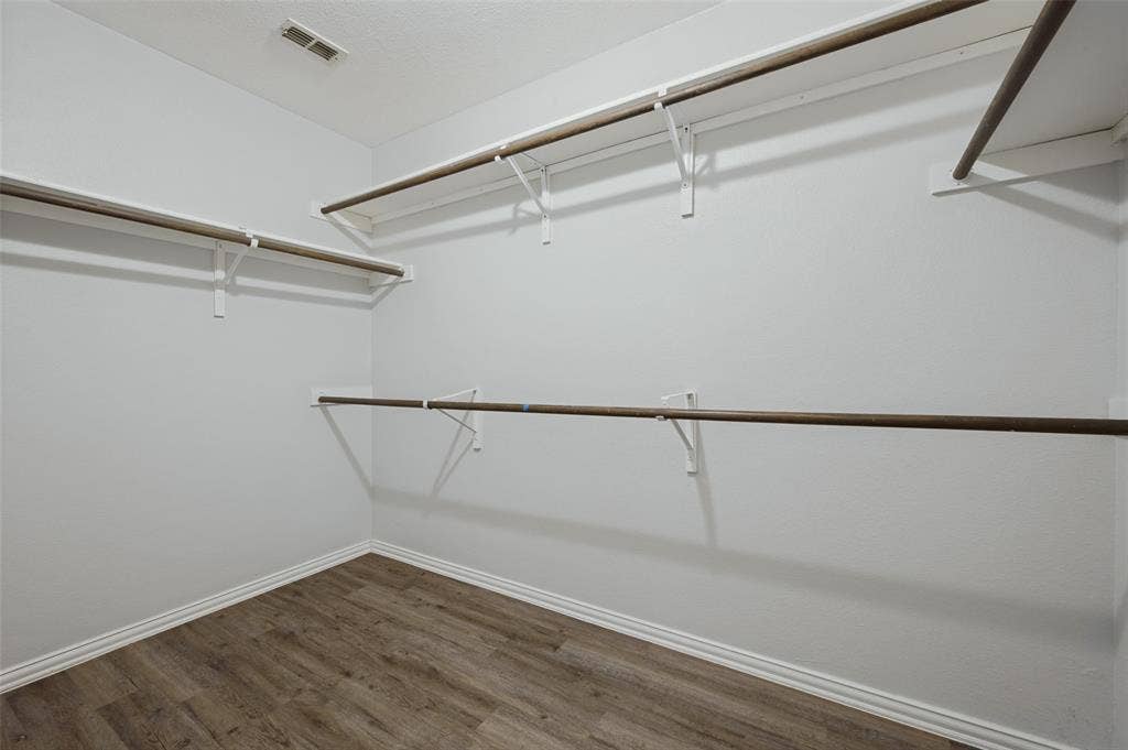 Walk-in storage area featuring wood-finish flooring and tiered, wall-mounted shelving with integrated hanging rods