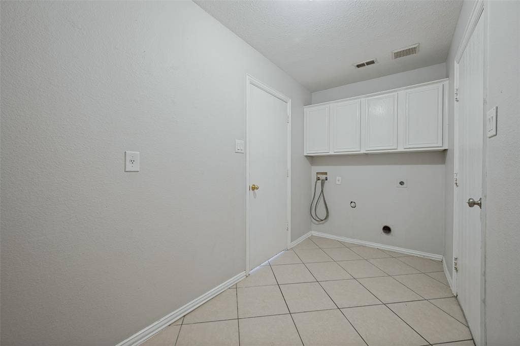 Utility area featuring light-toned tile flooring, white shaker-style wall-mounted cabinetry, and dedicated washer and dryer hookups