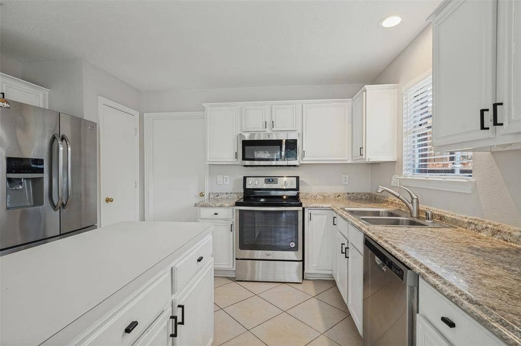 Kitchen featuring white cabinetry, stone-finish countertops, stainless steel appliances, a kitchen island, and ceramic tile flooring