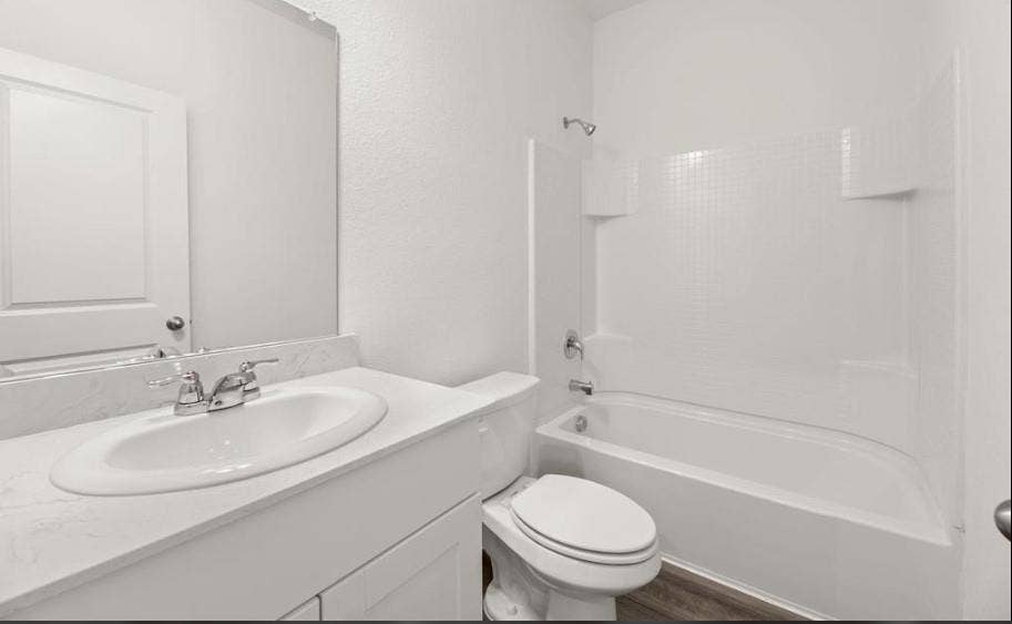 Bathroom featuring a vanity with a white countertop and oval under-mount sink, white paneled cabinetry, large wall-mounted mirror, and a tub-shower combination with a white surround
