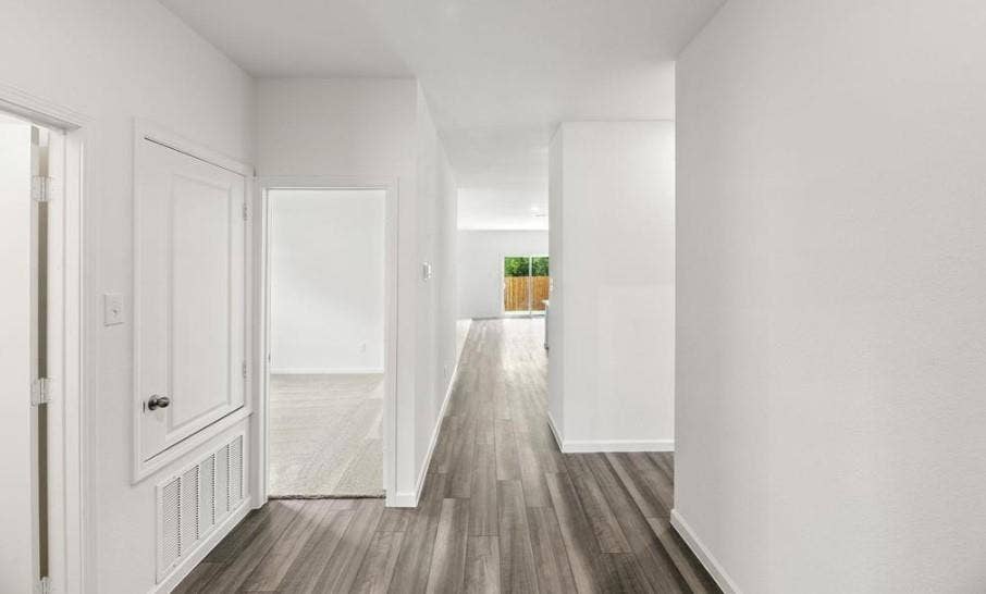 Hallway featuring wood-finish plank flooring, crisp white walls, and a recessed doorway