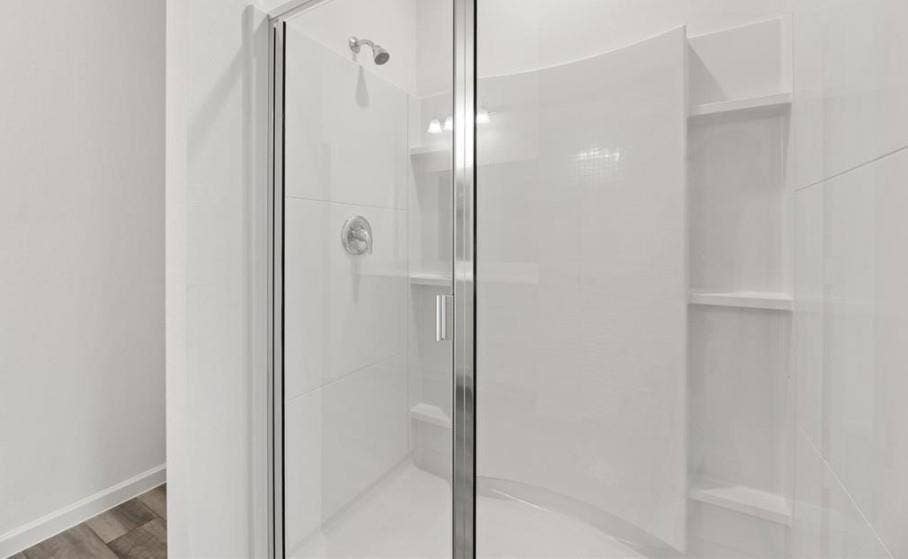 Walk-in shower featuring a curved glass enclosure, smooth white surround panels, integrated shelving, and a chrome shower fixture