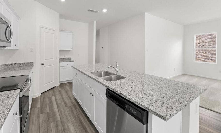 Kitchen featuring a central island with a double-basin stainless steel sink, speckled stone countertops, shaker-style white cabinetry, stainless steel appliances, and wood-finish flooring
