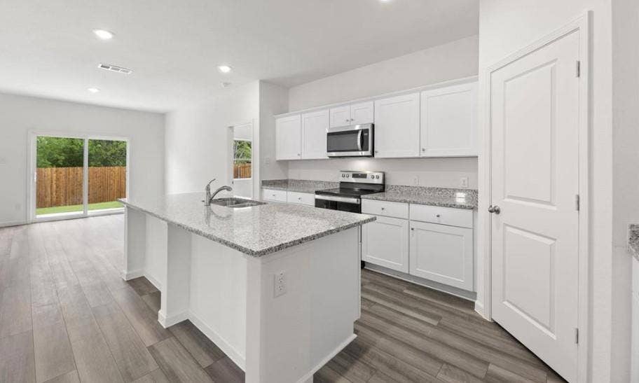 Kitchen featuring a central island with a stone-finish countertop, white cabinetry, integrated stainless steel appliances, and wood-finish flooring