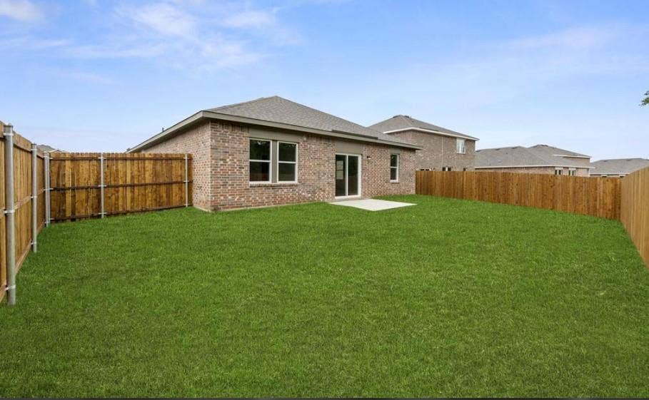 Rear exterior featuring a brick facade, concrete patio, and fenced-in backyard with a grass lawn