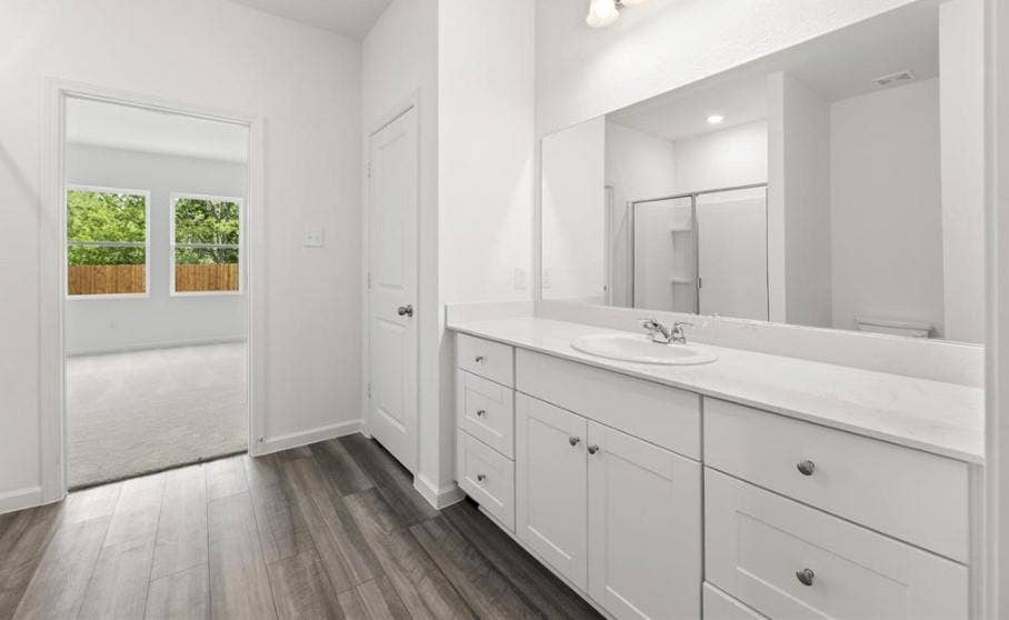 Bathroom featuring a white vanity cabinet with an integrated sink and solid-surface countertop, full-width vanity mirror, chrome-finish faucet, and wood-finish flooring