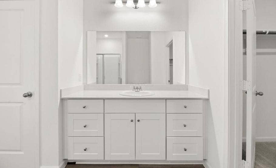 White vanity featuring shaker-style cabinetry, an integrated oval sink, solid-surface countertop, and a full-width wall mirror with a multi-bulb light fixture