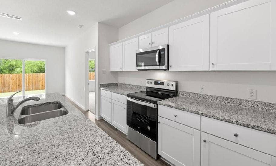 Kitchen featuring white shaker-style cabinetry, stone-finish countertops, stainless steel appliances, and a double-basin undermount sink