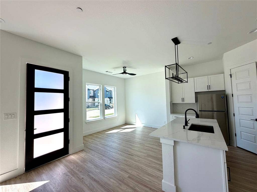 8902 Lowell Street, Rowlett, TX 75089 Open-concept interior featuring wood-finish flooring, a kitchen island with stone-finish countertops, matte black plumbing fixtures, white shaker-style cabinetry, and a multi-panel glass entry door