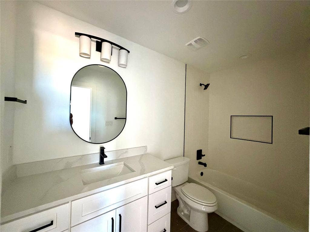8902 Lowell Street, Rowlett, TX 75089 Bathroom featuring a vanity with stone-finish countertop, undermount sink, matte black fixtures, oval wall mirror, and a built-in shower niche